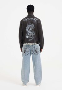 Black leather jacket with a dragon graphic on the back, paired with light blue jeans featuring spider web designs on the pockets.