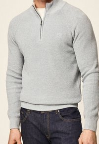 Maglione a coste grigio chiaro con collo a mezza zip indossato sopra una camicia bianca, abbinato a jeans blu scuro.