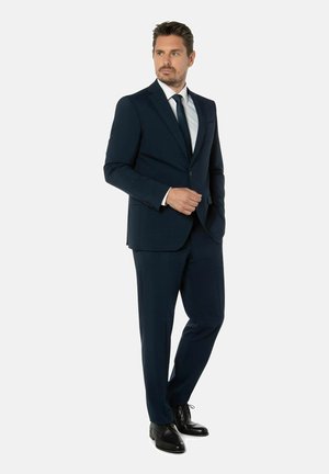 Marineblauer Anzug aus strukturiertem Stoff, mit Jacke mit einem Knopf und passender Hose, kombiniert mit einer schwarzen Krawatte und Schuhen.