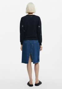 Felpa blu navy con ricami floreali sulle maniche, abbinata a una gonna di denim con uno spacco posteriore e una vita aderente. Sandali neri.