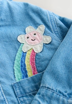 Buzunarul unei jachete din denim cu o floare brodată, cu o față roz și petale albe, deasupra unui curcubeu în culori pastelate, țesătură texturată.