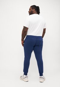 Mørkeblå joggebukser med elastisk midjebånd og mansjetter, kombinert med en enkel hvit t-skjorte. Joggesko med et lysegrått og hvitt design.