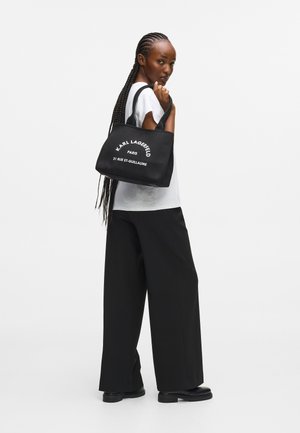 Must mustre bag, mille mustriga "KARL LAGERFELD PARIS 21 RUE ST-GUILLAUME" valges tekstis, mis on varustatud tugevate sangade ja kastja kujuga.