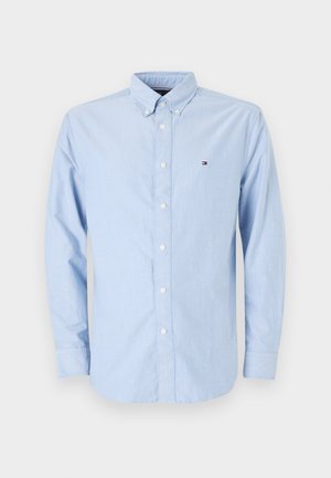 Light blue button-up shirt made of cotton. Features long sleeves, a collar, and a small embroidered logo on the chest. Plain fabric texture.