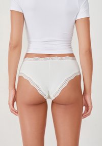 Lingerie bianca con bordo in pizzo, realizzata in un tessuto morbido e caratterizzata da un design a onde e una forma a copertura media sul retro.