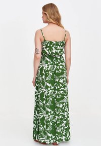 Maxikleid in Grün und Weiß mit dünnen Trägern, elastischem Taillenbund und fließender Silhouette, das Blattmuster und eine weiche Textur aufweist.