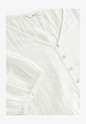 Fehér, rövid ujjú blúz V-nyakkal, gombos záródással és texturált anyaggal, amelyen apró kiemelkedő pöttyök találhatóak. Puha, könnyű anyag.