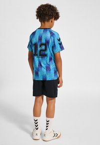 Blå och lila mönstrad sporttröja med nummer "12" på ryggen, ihop med svarta shorts. Vita strumpor med svart chevronmönster.