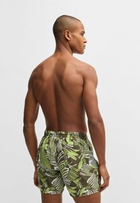 Green and white patterned swim shorts with an elastic waistband, featuring a tropical leaf design. The fabric appears lightweight and smooth.