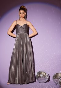 Metaliczna srebrna suknia z cienkimi ramiączkami, dopasowaną górą i plisowanym dołem. Posiada dekolt w kształcie serca i lustrzaną powierzchnię.