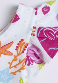 Bomullstopp med färgglada blommönster och abstrakta mönster; har volangkantade ärmslut; i huvudsak vit bakgrund med ljusa accenter.