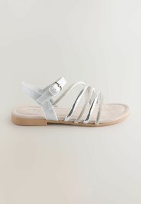 Zilveren sandaal met meerdere smalle banden, een gestrikte beige voetbed, een verstelbare enkelband en een platte lichtbruine zool.