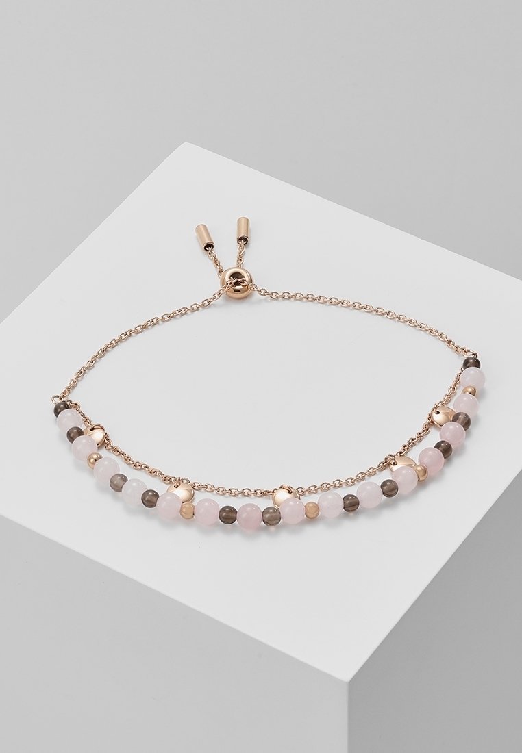 Bracelet chaîne en or rose avec curseur réglable, comportant des perles alternées roses, blanches, grises et de petits accents métalliques sur une surface grise.