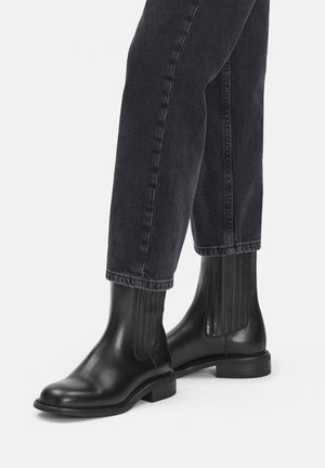 Czarne skórzane botki za kostkę z elastycznymi panelami, zaokrąglonym noskiem i niskim obcasem na słupku, zestawione z ciemnymi jeansami. Gładka i błyszcząca faktura.