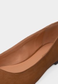 Chaussure plate en daim marron avec un bout arrondi et une semelle intérieure rembourrée sur un fond blanc uni.