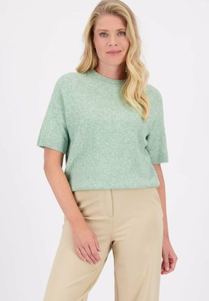 Korte mouwen, mintgroene gebreide trui met een ronde halslijn en een gestructureerd visgraatpatroon, gecombineerd met beige broeken.