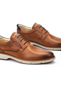 Zapatos de cuero marrón con un acabado suave, diseño de cordones, suela clara contrastante y detalles de costura sutiles en la parte superior.