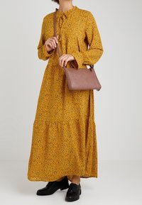 Gul blomstret maxikjole med lange ærmer og en volangkant, parret med en brun crossbody taske og sorte sko.
