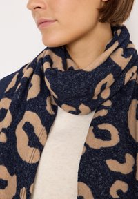 Marineblå og beige leopardmønstret tørklæde lavet af blødt stof, viklet omkring halsen, med en tekstureret finish og struktureret design.