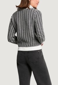 Maglione nero e bianco lavorato a maglia con motivo a rilievo, scollo rotondo e orlo bianco solido. Indossato con jeans grigio scuro.