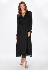 Schwarzes langärmeliges Kleid mit tiefem V-Ausschnitt, weichem Stoff und zarten gepunkteten Mustern. Fließender Rock mit tailliertem Detail.