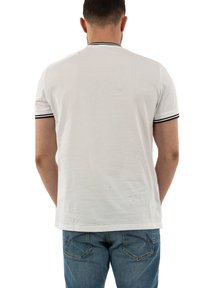 Camiseta blanca de algodón con cuello redondo y mangas cortas, con ribete negro en las mangas y el cuello, vista desde la parte posterior.