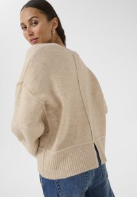 Maglione beige in lana con una vestibilità ampia, orlo a coste e fessure laterali; presenta una scollatura ampia e profonda e cuciture sulle spalle abbassate.