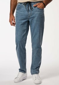 Joggers de mezclilla azul claro con cintura ajustable, bolsillos laterales y detalles de rayas en los muslos, combinados con zapatillas blancas.