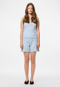 Gaiši zils adīts topiņš un atbilstošas šortus, ar ribotu tekstūru. Aksesuāri ietver vienkāršas auskari un tumšas plakanas kurpes.