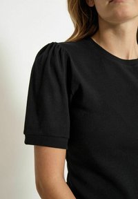 Zwarte geribbelde gebreide t-shirt met korte pofmouwen en een ronde halslijn. De stof heeft een gladde textuur met een lichte rek.