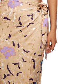Jupe portefeuille légère en satin beige ornée de motifs floraux et de points dorés. Dotée d'une ceinture latérale, d'une texture lisse et d'un tombé souple.