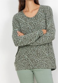 Hellgrüner Pullover mit dunkelbraunem Tiermuster, langen Ärmeln und Rundhalsausschnitt, kombiniert mit hellgrünen Hosen. Weicher Stoff ist sichtbar.