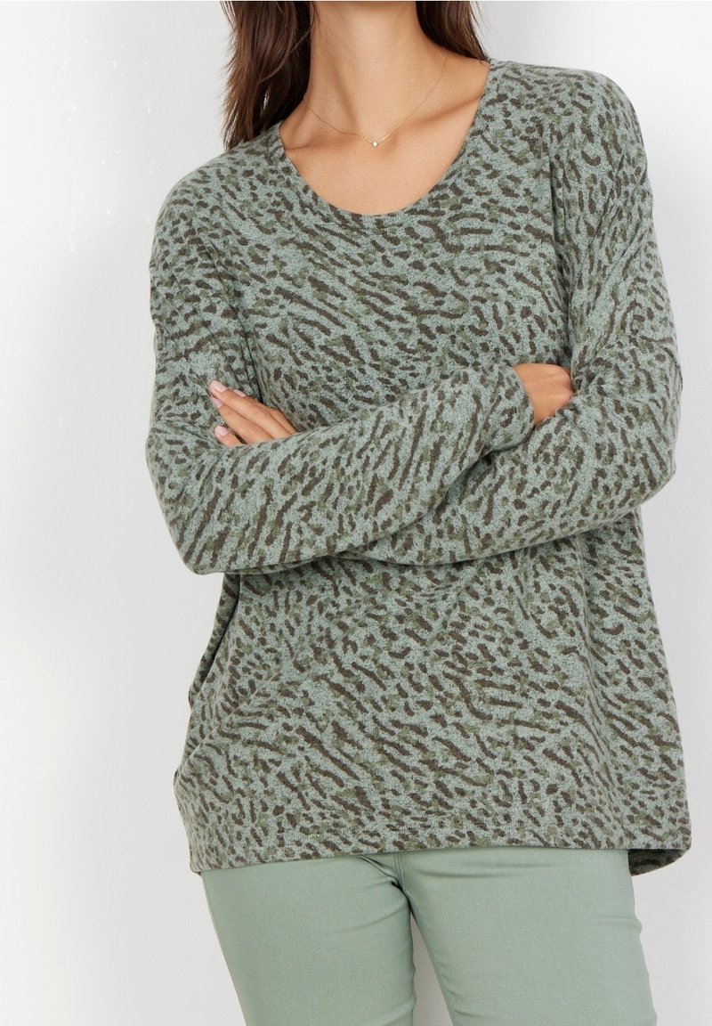 Hellgrüner Pullover mit dunkelbraunem Tiermuster, langen Ärmeln und Rundhalsausschnitt, kombiniert mit hellgrünen Hosen. Weicher Stoff ist sichtbar.