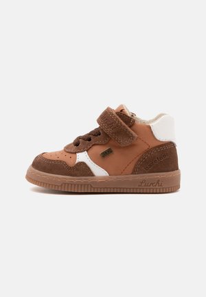 Brun og hvid sneakers til småbørn med velcrobånd, snøres detaljer, gummisål og blødt polstret krave vist fra siden på en ensfarvet baggrund.