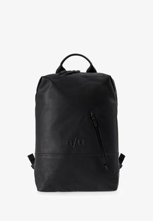 Man and woman wearing casual clothes, each carrying a black backpack, standing and looking toward the camera on a white background.