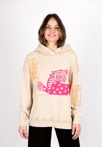 Beige oversized hoodie with a kangaroo pocket. Features colorful graphic of a tiger and text in orange, pink, and stars. Soft material.