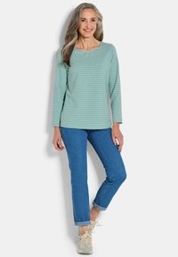 Lange mouwen, lichtblauwe gestreepte top met een ronde hals, gecombineerd met blauwe jeans. Afgerond met opgerolde manchetten en lichte sneakers.