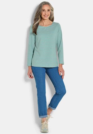 Lange mouwen, lichtblauwe gestreepte top met een ronde hals, gecombineerd met blauwe jeans. Afgerond met opgerolde manchetten en lichte sneakers.