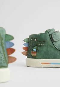 Grüne Ledersneaker mit einem Krokodil-Design und mehrfarbigen Stacheln an der Ferse. Ausgestattet mit einem Klettverschluss und einer strukturierten Gummisohle.