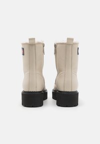 Botas de tobillo de cuero color crema con forro de pelo sintético, parte superior texturizada, suela gruesa negra y un parche con el logo en el talón.
