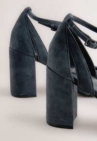 Donkerblauwe suède sandalen met hoge blokhakken, een open ontwerp en verstelbare enkelbandjes, met een gelaagde textuur.