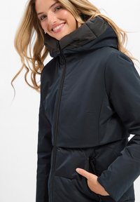Donkerblauwe gewatteerde jacket met een hoge kraag, voorzien van een ritssluiting en zijzakken, gemaakt van glad, waterafstotend materiaal.