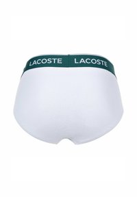 Slip en coton blanc avec une ceinture verte arborant "LACOSTE" en texte blanc, texture lisse et design simple.