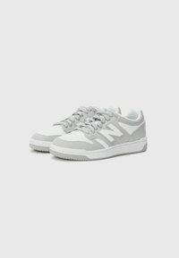 Grå och vita sneakers med en texturerad ovandel, perforeringar för andningsförmåga och en framträdande "N"-logotyp på sidan, med en flat sula.