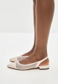Ballerine beige con tomaia in rete e punta appuntita. Il design include un tacco basso e un retro aperto per una facile calzata.