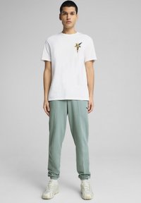 Hvid bomulds t-shirt med grafisk design og gyldne detaljer, sammen med lysegrønne sweatpants og lyse sneakers.