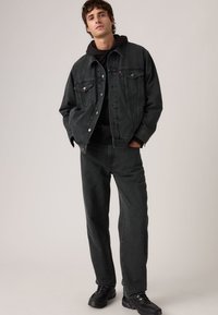 Μαύρο τζιν μπουφάν με κάθετη ραβδωτή υφή, συνδυασμένο με μαύρο τζιν παντελόνι και μαύρη φούτερ με κουκούλα. Διαθέτει ασημί κουμπιά και τσέπες.