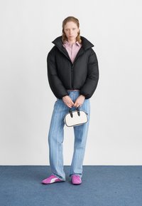Čierna nafúknutá bunda s vysokým golierom, ružová košeľa s gombíkmi, svetlomodré pruhované džínsy a ružové športové topánky. Malá biela kabelka s čiernymi akcentmi.