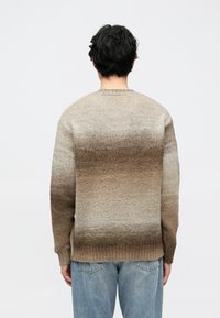 Stickad tröja med en gradient från ljus beige till mörkbrun, med ribbad rund halsringning och muddar, mot en neutral bakgrund.