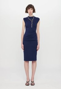 Costum din două piese de culoare bleumarin, format dintr-o bluză ajustată cu mâneci scurte și o fustă creion. Include un accent din lanț la guler.